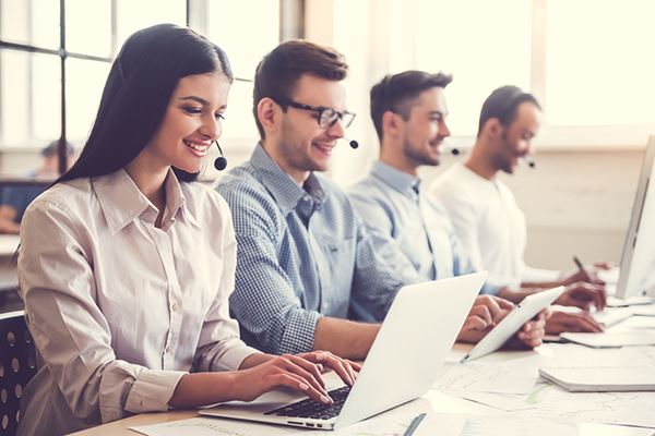 A group of customer service representatives sit in an open-office work station.