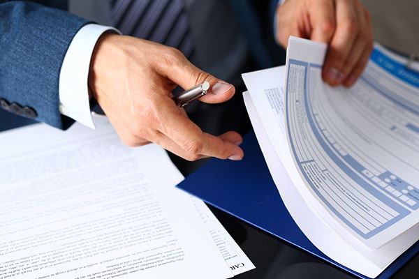 A man in a suit ruffles through a stack of forms.