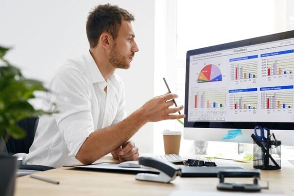 A young businessman looks at charts and graphs on his computer monitor.