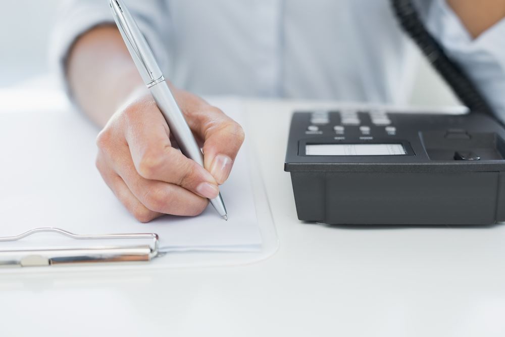 person on the phone while taking notes on paper